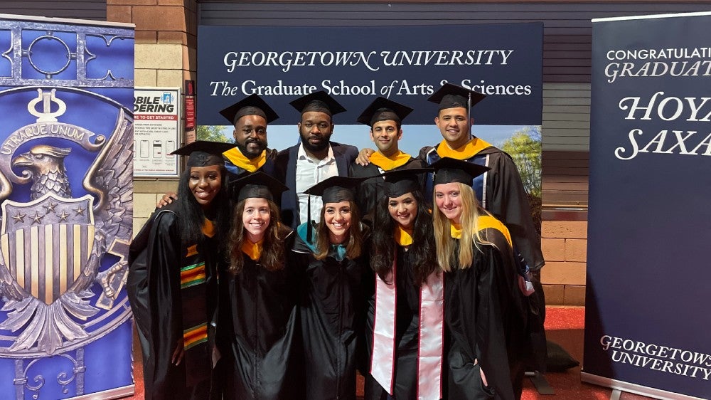 Systems Medicine graduates pose together in their regalia in front of Georgetown banners